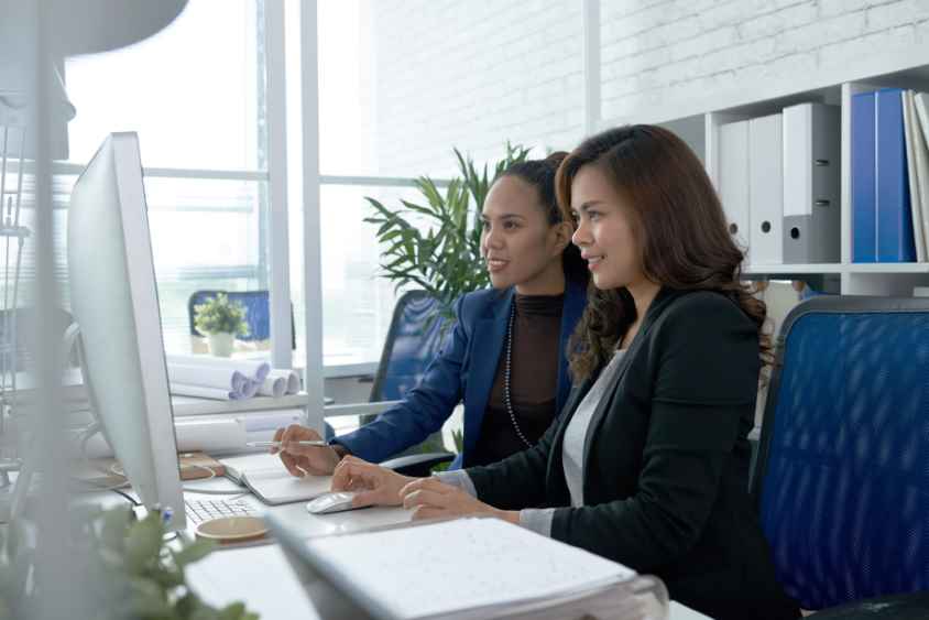 Smiling Filipino business women working on computer togetehr